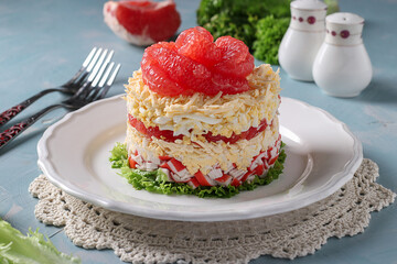Festive salad with grapefruit, cheese and crab sticks on a white plate on blue background © Anzhela