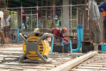 Yellow concrete vibrater on rebar for floor pouring frame in construction area, background with columnar and building condition during construction.