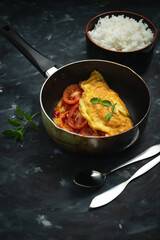 Breakfast omelet with tomatoes and rice on a dark background