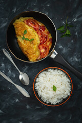 Breakfast omelet with tomatoes and rice on a dark background