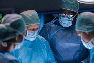 Multiracial team of professional medical surgeons performs the surgical operation in a modern...