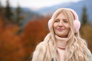Young beautiful woman wearing warm earmuffs in mountains - obrazy, fototapety, plakaty