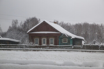An abandoned old house in the village in winter in the snowfall. Lack of properte. Russia.