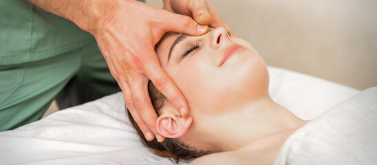 Pretty young caucasian woman receiving a head massage by a male massage therapist in a beauty salon