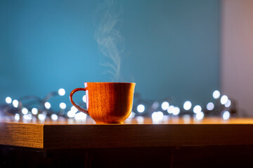 Wooden mug with coffee. Steam comes from the cup from hot coffee, chocolate, tea. Christmas lights...