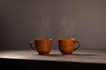 Wooden mug with coffee. Steam comes from the cup from hot coffee, chocolate, tea. Christmas lights in the background. Christmas is coming soon