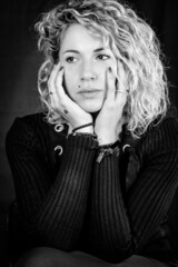 Black and white portrait of a beautiful young woman with blond curly hair holding her face with her hands as she sadly looks to the side