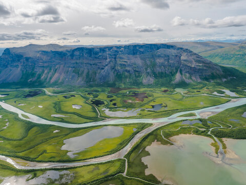 Aerial scenic view from Skierffe rock summit on glacial Rapadalen river delta valley at Sarek national park with meanders, lakes, mountains and birch trees. Summer day landscape Sweden Lapland