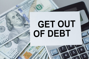 On the table money and a calculator and a card with the words GET OUT OF DEBT on it. Business concept