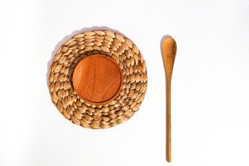 a wooden placemat on top of the wicker placemat and a wooden spoon beside on white. a flat lay shot...