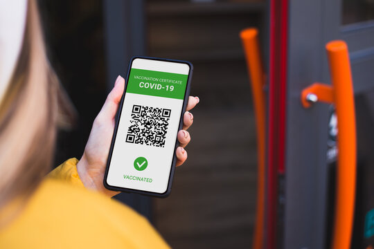 Young woman holding mobile phone with online Covid-19 vaccination certificate opens cafe door