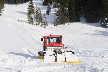 red tractor of municipal service in mountains of Swiss Alps with wide snow shovel clears the road...