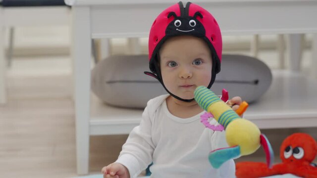 Baby sitting on the floor playing with toys, cute little baby boy wearing soft safety helmet learning to crawl and sit, head protector for crawling walking helps reduce impact of falls.