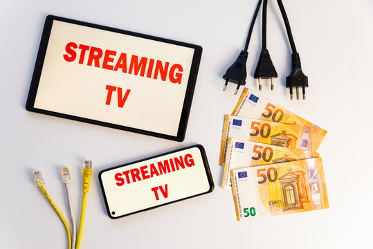 Tablets and smartphones showing the text "streaming tv" on the display, banknotes, data cables, money and electrical plugs. Costs and consumption of streaming TV programs. 