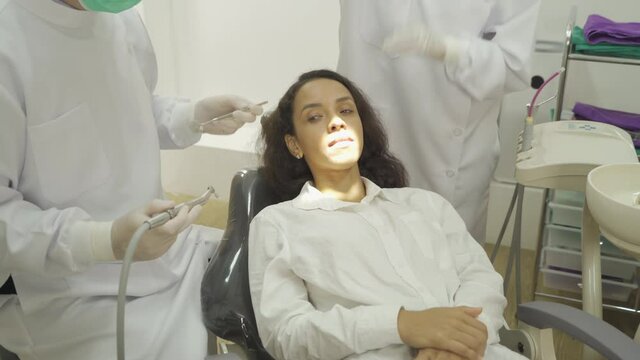 A dentist checking up Latin woman's teeth by using dental mouth mirror at hospital clinic. Teeth check up with dental tools. Doctor. Dentistry, medical and health. People.