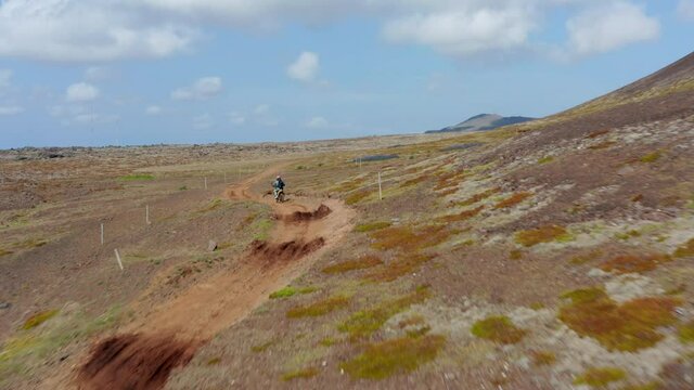 Aerial view following man doing motocross over hill on Iceland. Drone view of biker riding on dirt road among mountains