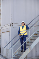 Full length of mature man factory worker holding cup of coffee and talking on cellphone