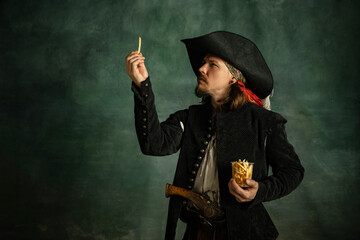 Portrait of one brutal man, medeival pirate holding fries isolated over dark background.