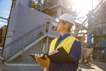 Joyful matured man holding folder with documents and smiling while standing on territory of...