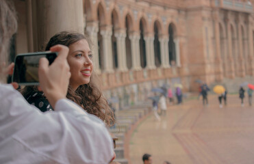 Young girl poses smiling while her friend takes a picture of her in Plaza of Spain in Seville to post on her social media