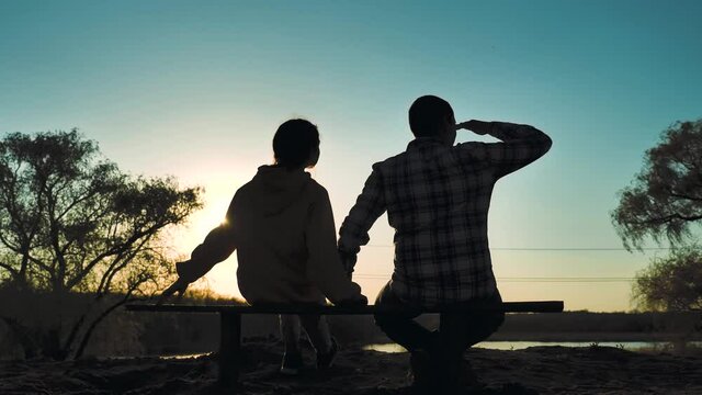 happy family man and girl teamwork sitting on a bench silhouette sunset in the park and nature. dad lifestyle and daughter relax in the park spend together. couple in love hold hand sit back look at
