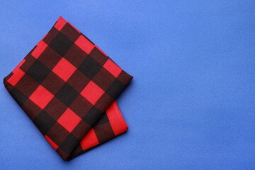 Folded red bandana with check pattern on blue background, top view. Space for text