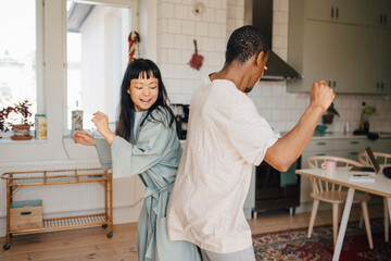 Joyful female and male friend dancing at home