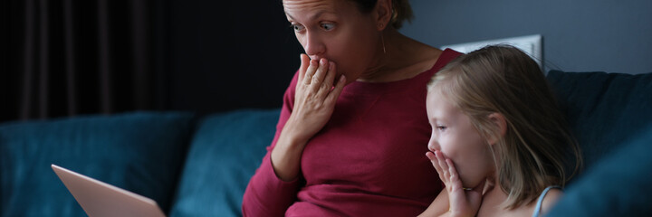 Shocked surprised mom and daughter looking at laptop screen while sitting on couch