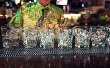 Cocktail glass with ice cubes on counter bar in nightclub