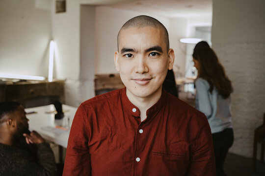 Portrait of smiling male hacker with colleagues in background at office