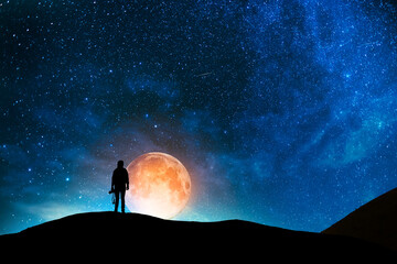 Fantasy night scene, photographer silhouette stands on hill and looks at the huge bright moon.