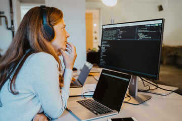 Mature female hacker brainstorming while coding over computer in office