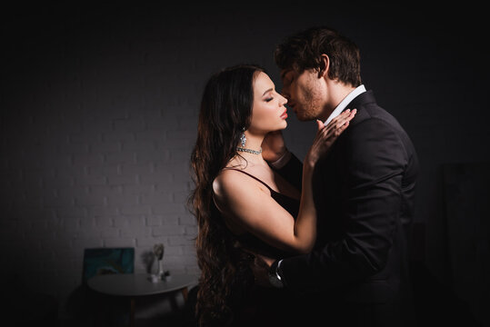 side view of young elegant couple embracing at home in dark bedroom