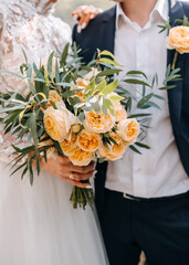Closeup of a couple of bride and groom holding bridal bouquet of pale orange roses.