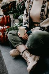 Closeup of a woman sitting on stairs outdoors with a blank cup of coffee to go.