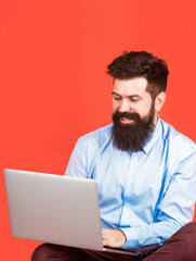 Happy young man sitting on the floor with and using laptop computer on red background. Holding laptop computer