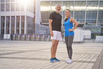 Active and beautiful middle aged couple in sportswear doing sports together in the city, standing...