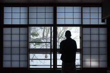 Man wearing yukata in traditional Japanese inn (Ryokan) enjoying winter snow...