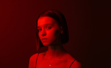 Close-up portrait of beautiful woman with square hairstyle in red neon light on wall background,...