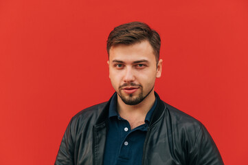 Portrait of handsome macho man with beard on red wall background, looking at camera with grin.