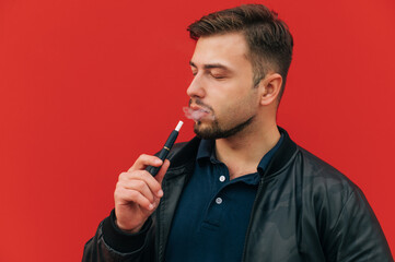 Handsome adult man with a beard smokes an electron cigarette with the evaporation of tobacco on a...