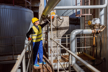Full length of matured man wearing safety helmet and vest while standing on metal bridge at manufacturing plant