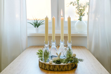 alternative advent wreath, candles in bottles on a wooden board with decoration on a table at the window, one is lit, first sunday before christmas, copy space