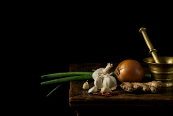 Obraz na płótnie Canvas Still life of dried chilis, garlic, ginger spring onion and onion on wooden table against black background