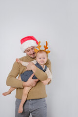 A smiling funny baby wearing deer antler headband being hold by father. Christmas costumes.