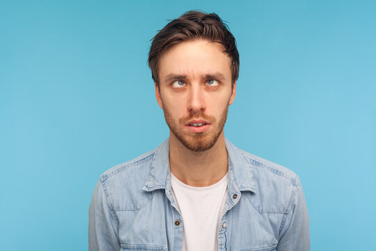 Portrait of comic positive handsome man wearing denim shirt, looking cross-eyed, having fun with silly face expression, playing fool. Indoor studio shot isolated on blue background.