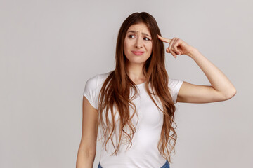 Portrait of displeased woman showing stupid gesture, accusing dumb reckless suggestion, crazy plan for idiots, wearing white T-shirt. Indoor studio shot isolated on gray background. - obrazy, fototapety, plakaty