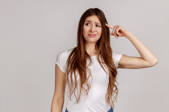 Portrait of displeased woman showing stupid gesture, accusing dumb reckless suggestion, crazy plan for idiots, wearing white T-shirt. Indoor studio shot isolated on gray background.
