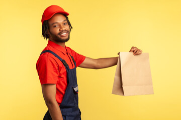 Side view portrait of happy professional courier wearing overalls giving groceries bag, delivering...