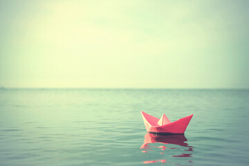 Pink paper boat floating on river. Retro photo effect